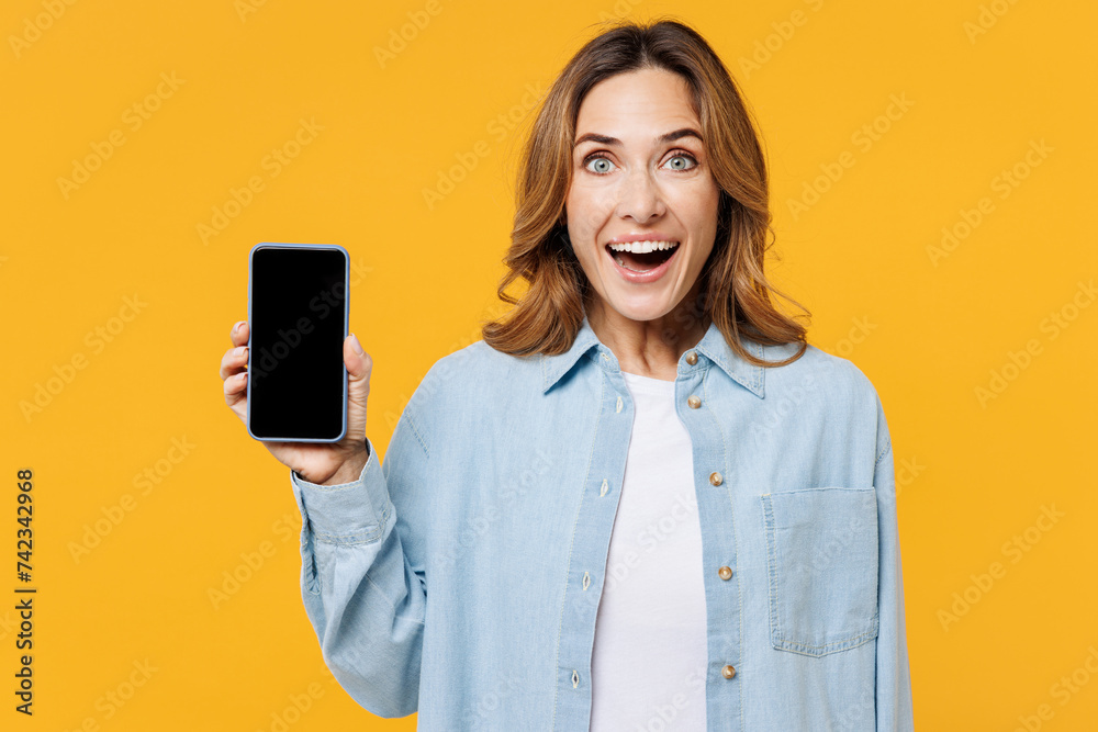 Young surprised woman she wear blue shirt white t-shirt casual clothes hold in hand use mobile cell phone with blank screen workspace area isolated on plain yellow background studio Lifestyle concept Young surprised woman she wear blue shirt white t-shirt casual clothes hold in hand use mobile cell phone with blank screen workspace area isolated on plain yellow background studio Lifestyle concept