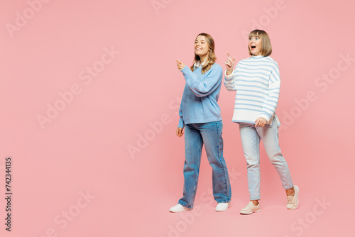 Full body happy cheerful elder parent mom with young adult daughter two women together wear blue casual clothes walk go point aside isolated on plain pastel light pink background. Family day concept.