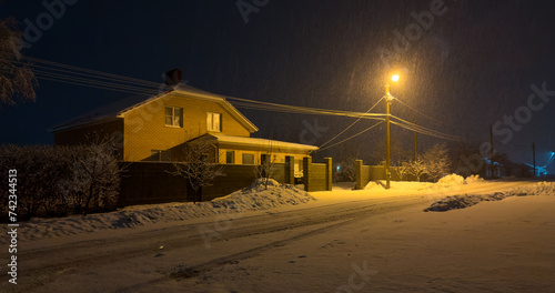 Snow falls in the light of a street lamp near the road at night