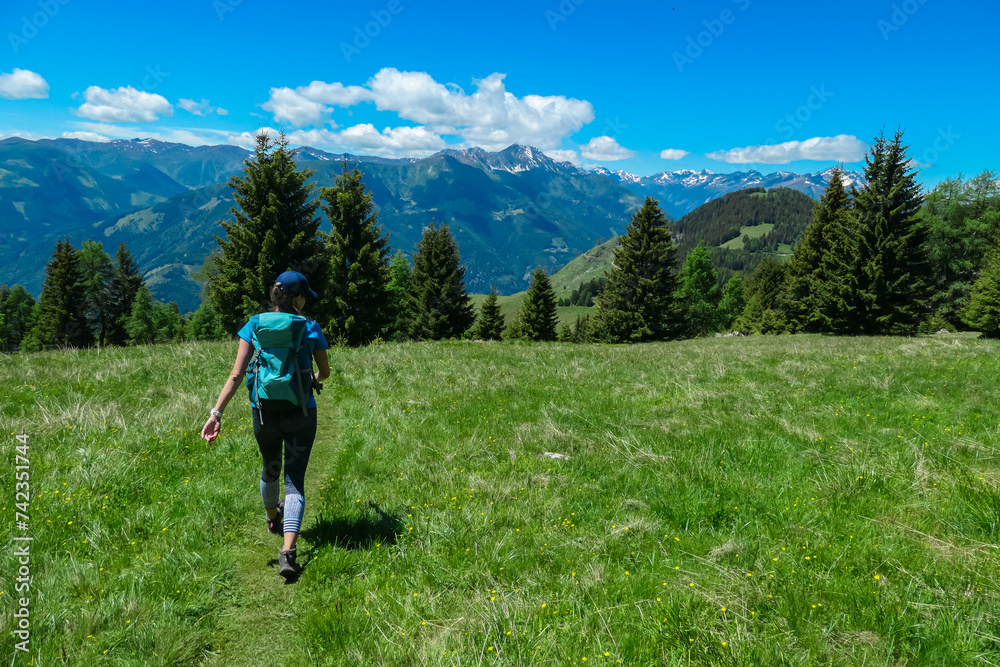 Hiker woman on alpine meadow with scenic view of majestic mountain peaks Carnic andd Julian Alps. Idyllic hiking trail to Boese Nase, Ankogel Group, Carinthia, Austria. Remote Austrian Alps in spring