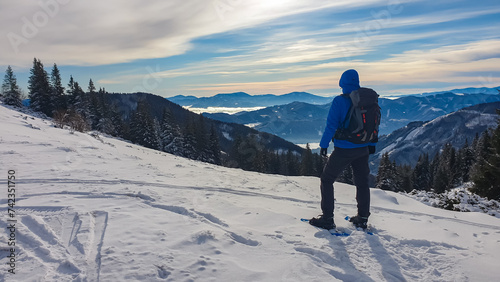 Man with snowshoes in snow covered meadow on way to Hochanger, Muerzsteg Alps, Styria, Austria. Panoramic view of snow capped mountain peaks Hochschwab massif. Winter wonderland remote Austrian Alps photo