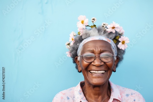An elderly African American woman, aged 70, smiling with easter bunny ears on her head, against a soft pastel blue backdrop, leaving space for text or design elements photo