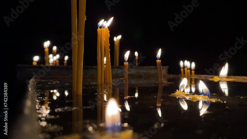 A row of candles casting reflections on a shiny surface, creating a peaceful and meditative ambiance. 