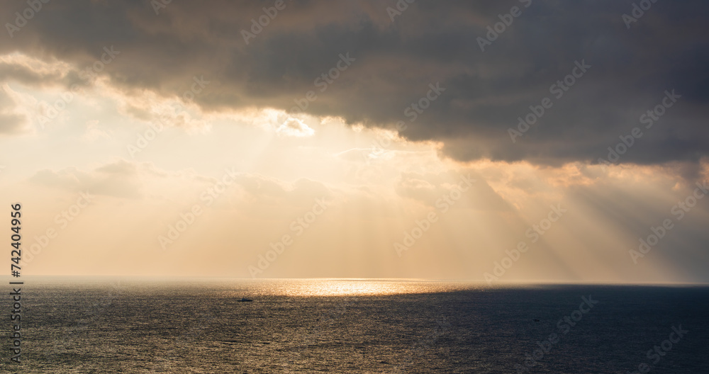 Majestic ocean sunrise scenery with sunlight shining through dark clouds