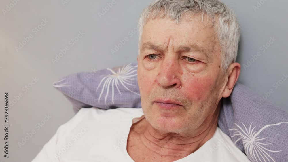 Serious concentrated Caucasian mature gray haired man in white T-shirt lying in bed with pensive expression unable to find relief from his insomnia in his bedroom Serious concentrated Caucasian mature gray haired man in white T-shirt lying in bed with pensive expression unable to find relief from his insomnia in his bedroom