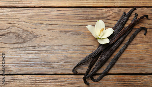 Vanilla sticks and flower on wooden background, flat lay; space for text