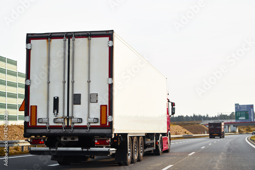 Semitrailer trucks transporting cargo on the highway. The trucks are delivering goods by land from door to door. They are part of a global sustainable logistics industry that supports trade commerce © AlexGo