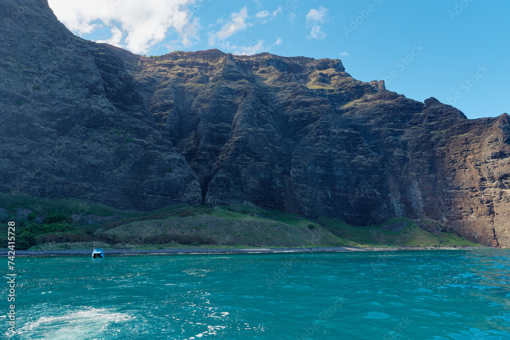 Amazing view of a peaceful bay and a small boat at Napali Coast State Wilderness Park from a tourist boat, Island of Kauai, Hawaii