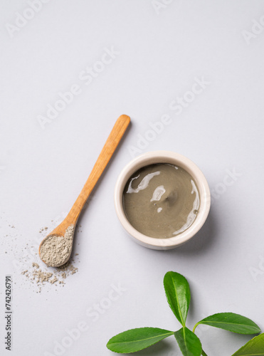 Blue clay in a bowl and spoon on a light background with leaves.