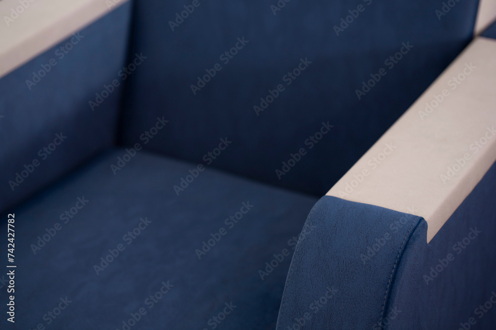 Close-up of an upholstered armchair made of a combined blue and beige fabric. A piece of upholstered furniture for relaxation and sleep made of dark blue velor with fine pile and a blurred background. Close-up of an upholstered armchair made of a combined blue and beige fabric. A piece of upholstered furniture for relaxation and sleep made of dark blue velor with fine pile and a blurred background.