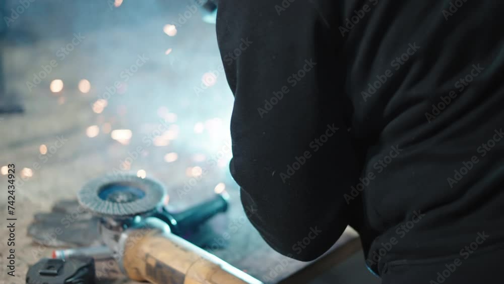 Industrial workman in protective gloves, uniform and welding helmet welding metal with flashing electrodes in workshop, blacksmith forming constructional frame or creating other metal product Industrial workman in protective gloves, uniform and welding helmet welding metal with flashing electrodes in workshop, blacksmith forming constructional frame or creating other metal product