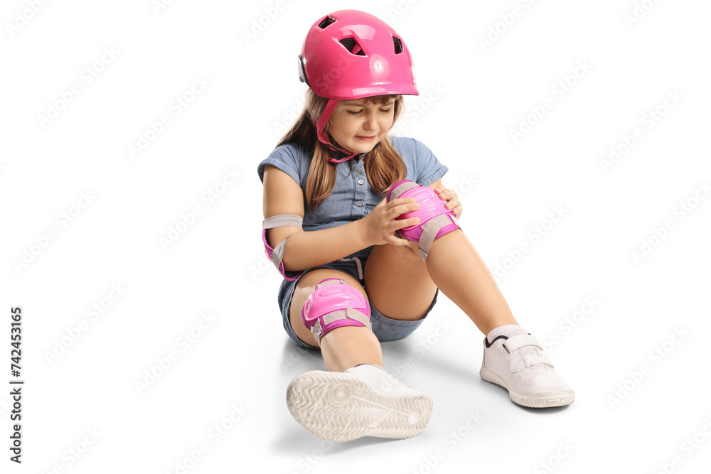 Sad little girl with pads and helmet sitting on the floor with injured knee Sad little girl with pads and helmet sitting on the floor with injured knee
