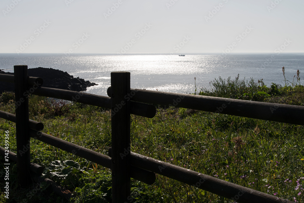 View of the sea with sunlight reflection over the wooden fence