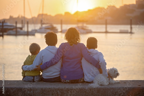 Children, boys, brothers, enjoying sunset over river with their pet maltese dog and mom, boats, sun, river photo