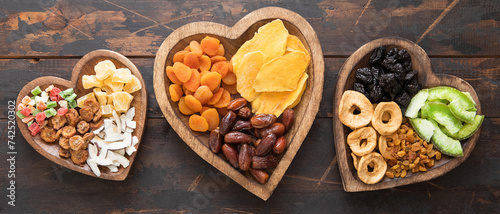 Healthy sweet dried fruits and berries in wooden heart shaped plates on wooden background.Top view.