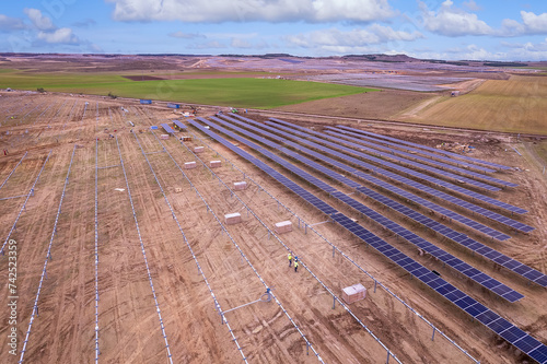 Elevated view of a large photovoltaic power plant under construction with many rows of solar panels and rows of metal frame ready for installing panels for producing Green Energy. Agrivoltaics concept