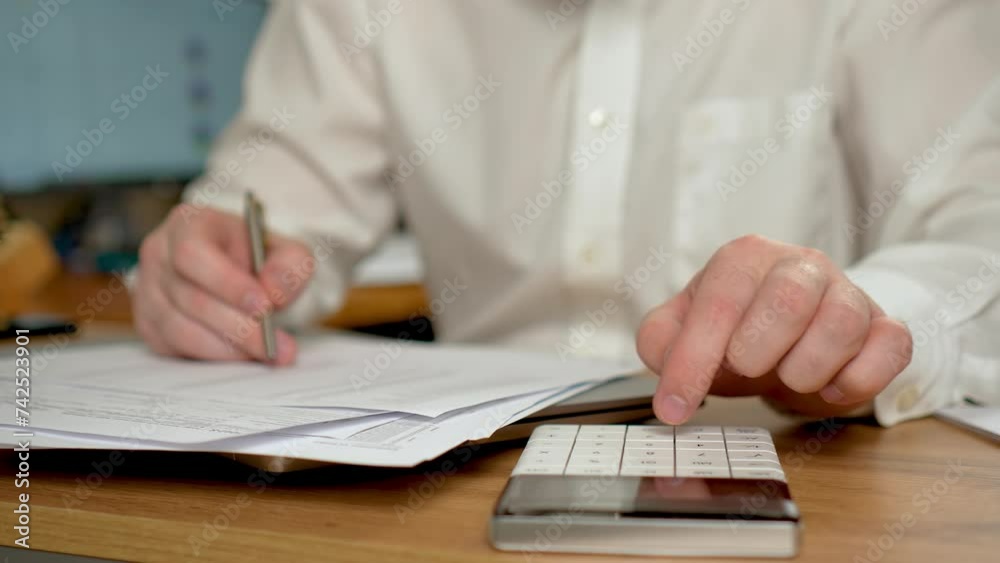 Man using calculator close up, doing math finance on office desk, tax, report, accounting, statistics and analytical research. Male professional using computer modern notebook sitting at home office Man using calculator close up, doing math finance on office desk, tax, report, accounting, statistics and analytical research. Male professional using computer modern notebook sitting at home office