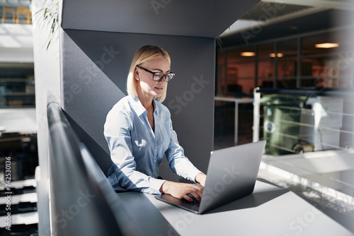 Concentrated busineswoman working online in an office pod on her laptop in a office community photo