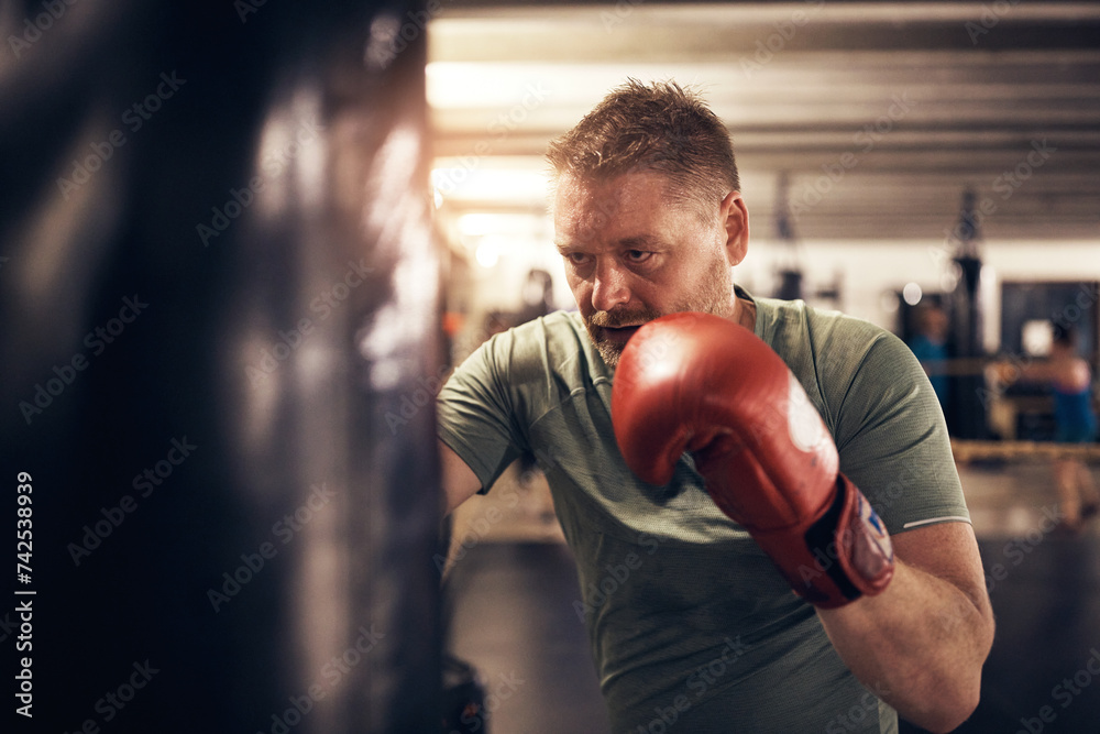 Mature man hitting a punching bag during a boxing gym workout class Mature man hitting a punching bag during a boxing gym workout class