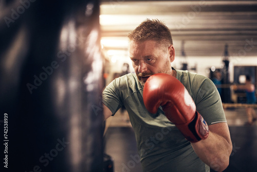 Mature man hitting a punching bag during a boxing gym workout class photo