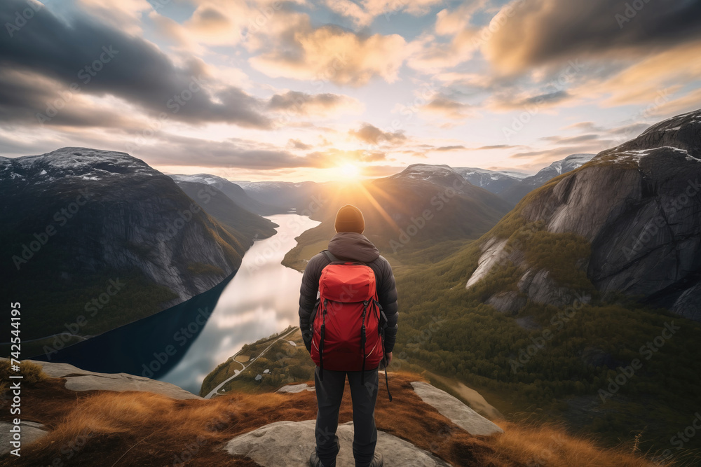 Back view of tourist standing on top of a rock and enjoying fascinating view with mountains and lakes around. Concept of adventure in Scandinavian countries - obrazy, fototapety, plakaty 