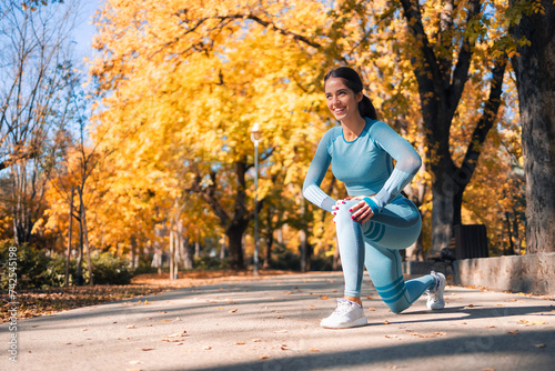 A smiling athletic young woman kneeling and stretching her legs in the park before her routine run