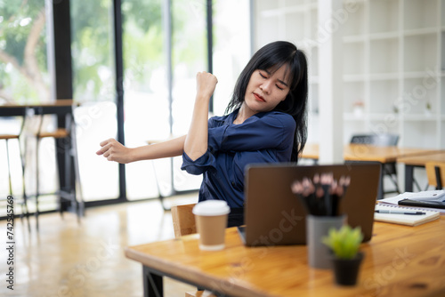 A female employee stretching lazy at the desk to relax while working in the office. Feeling stressed and achy from work.