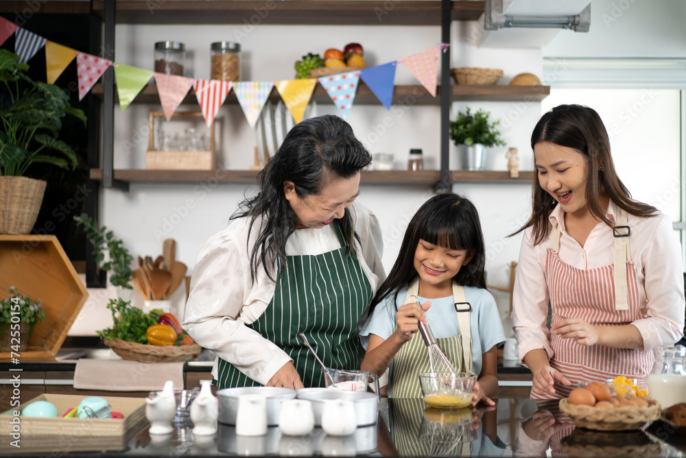 Asian female baker pastry chef mother and old senior grandmother helping teaching little girl daughter niece standing smiling holding using sieve sifting flour powder into glass bowl preparing dough