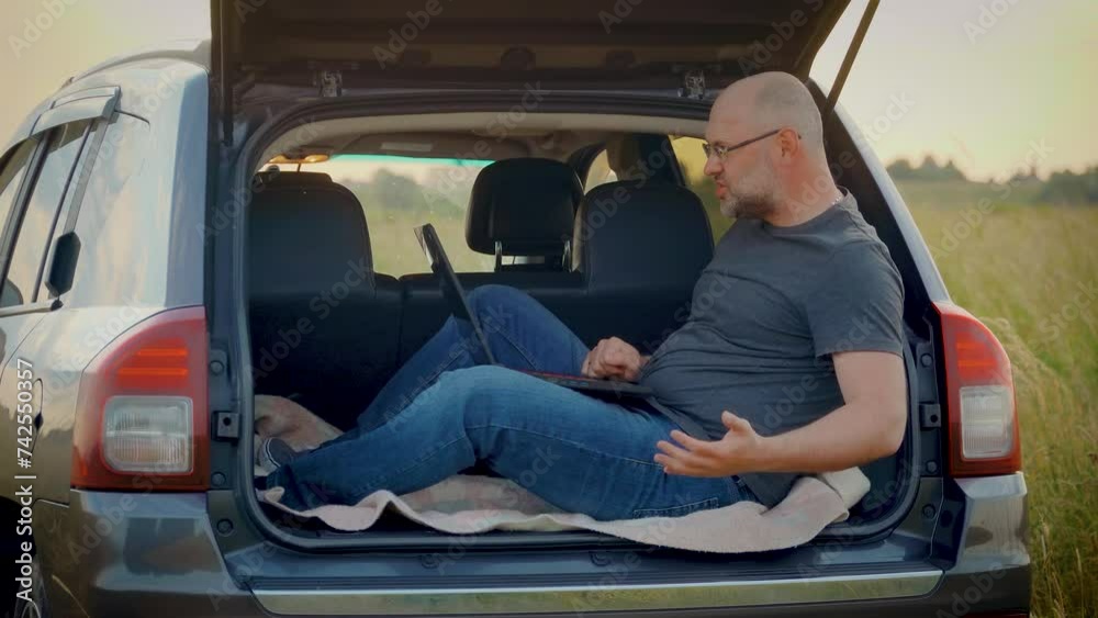 Man remotely emotionally talking by corporate video chat waving having hands working on laptop sitting in car trunk while traveling. Busy worker freelancer entrepreneur notebook online working Man remotely emotionally talking by corporate video chat waving having hands working on laptop sitting in car trunk while traveling. Busy worker freelancer entrepreneur notebook online working