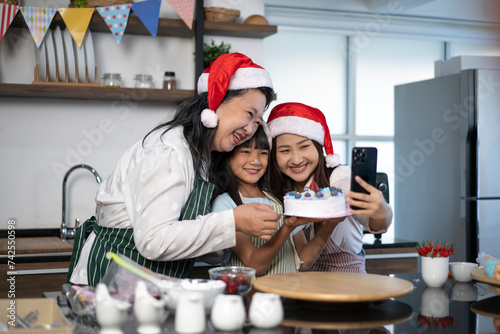 Happy Grandmother, mother and little daughter taking photo through smartphone while finish decorated cake for Christmas day. Three generations Asian women taking selfie through smartphone