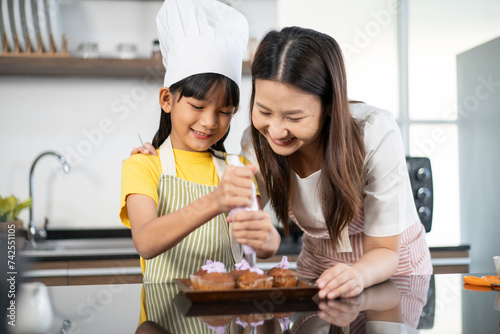 Asian beautiful female mother helping teaching little girl daughter holding pan sifting flour into glass bowl preparing to baking homemade bakery dough cake pie together in decorated kitchen at home