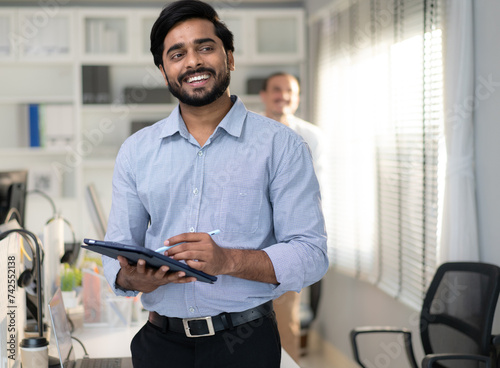 Indian businessman happy working in corporate office. Confident smart bearded man entrepreneur hold clipboard smiling looking. Friendly India ethnic executive boss manager working his job in workplace