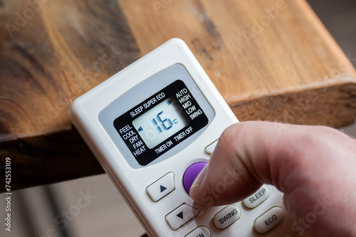 Finger of a man using the control of an air conditioner that reads sixteen degrees.