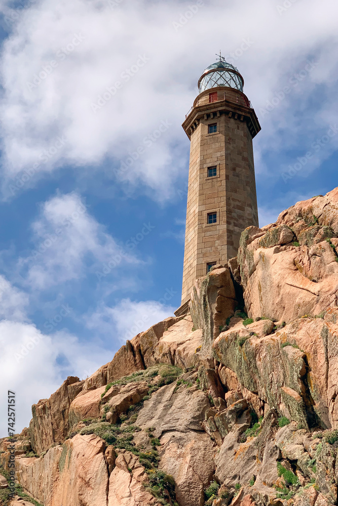 lighthouse on a rock against a background of blue sky with clouds