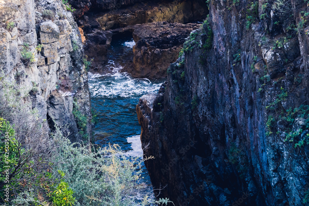 Gorge between rock walls and ocean waters below hitting white waves at the foot, selective focus.