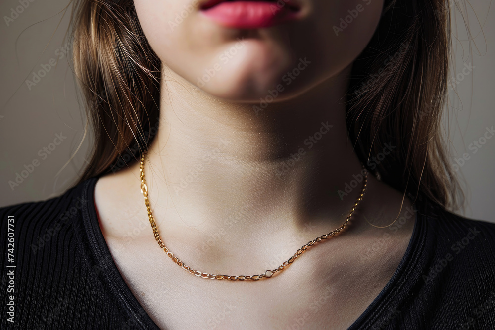 Close-up of a young woman wearing an elegant golden chain necklace on a neutral background