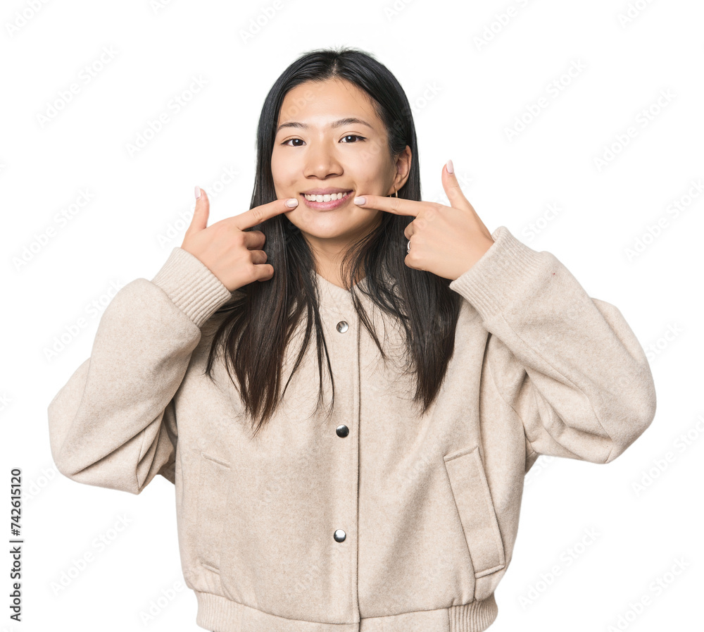 Young Chinese woman in studio setting smiles, pointing fingers at mouth. Young Chinese woman in studio setting smiles, pointing fingers at mouth.