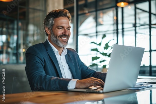 Smiling mature adult business man executive sitting at desk using laptop. Happy professional mid aged businessman ceo manager working on computer technology looking at laptop, Generative AI © Media Masterpieces
