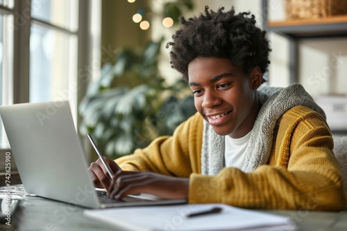 Happy African American teen student elearning at home on pc, writing notes. Smiling teenage boy using laptop watching webinar, hybrid learning english, Generative AI
