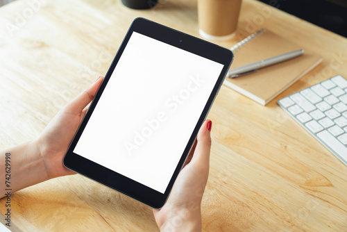 Hands holding digital tablet with mockup of blank screen on desk in office room.