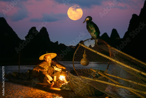 Obraz na płótnie Traditional Chinese Fisherman taking a break on bamboo raft with two cormorants
