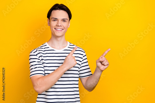 Portrait of toothy beaming student wear stylish t-shirt indicating at discount empty space isolated on bright yellow color background