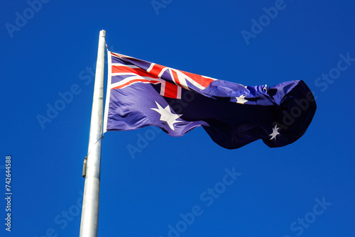 Australian flag floating in the wind at the top of a flagpole against a blue sky background