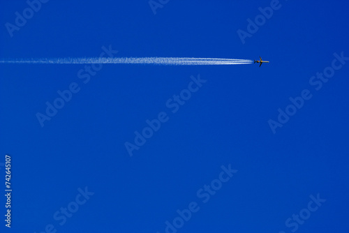 a passenger plane with vapour trails high in the blue sky