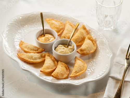 Hot Appetizers with Mini Chebureki and sauces Isolated on white table background. Restaurant Starter Menu with Crispy Burnt Turnovers, Pies or Samosa with Spicy Sause Close Up