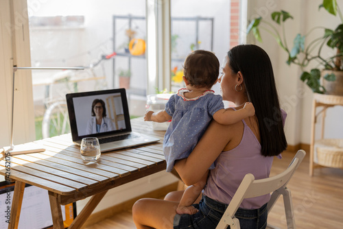 mother on her back with her daughter in her arms sitting on a video call with the doctor - virtual appointment, medicine at home