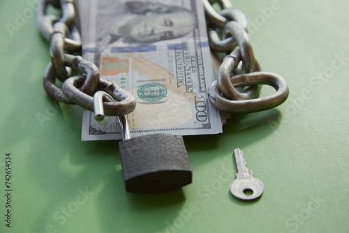 Fotografie Hundred-dollar bills with a chain on them and an open lock and key nearby on gr