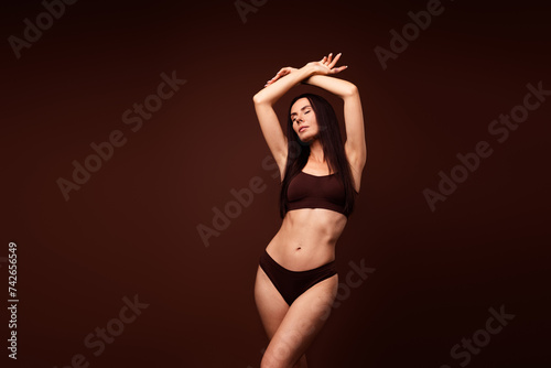 No filter photo of adorable dreamy tender girl posing with raised hands wearing top panties lingerie isolated on brown color background © deagreez
