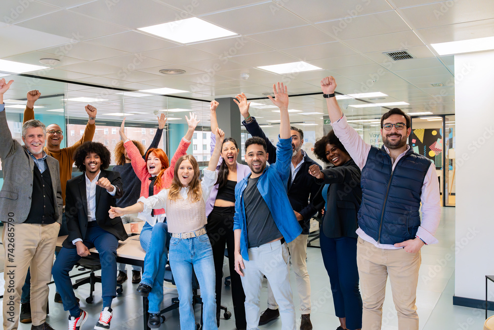 Naklejka premium An enthusiastic team of office workers celebrating with raised arms in a vibrant coworking space.