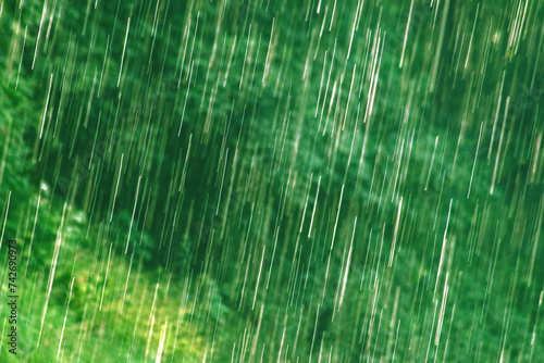 many bright raindrops of a rain shower against green background  motion blur